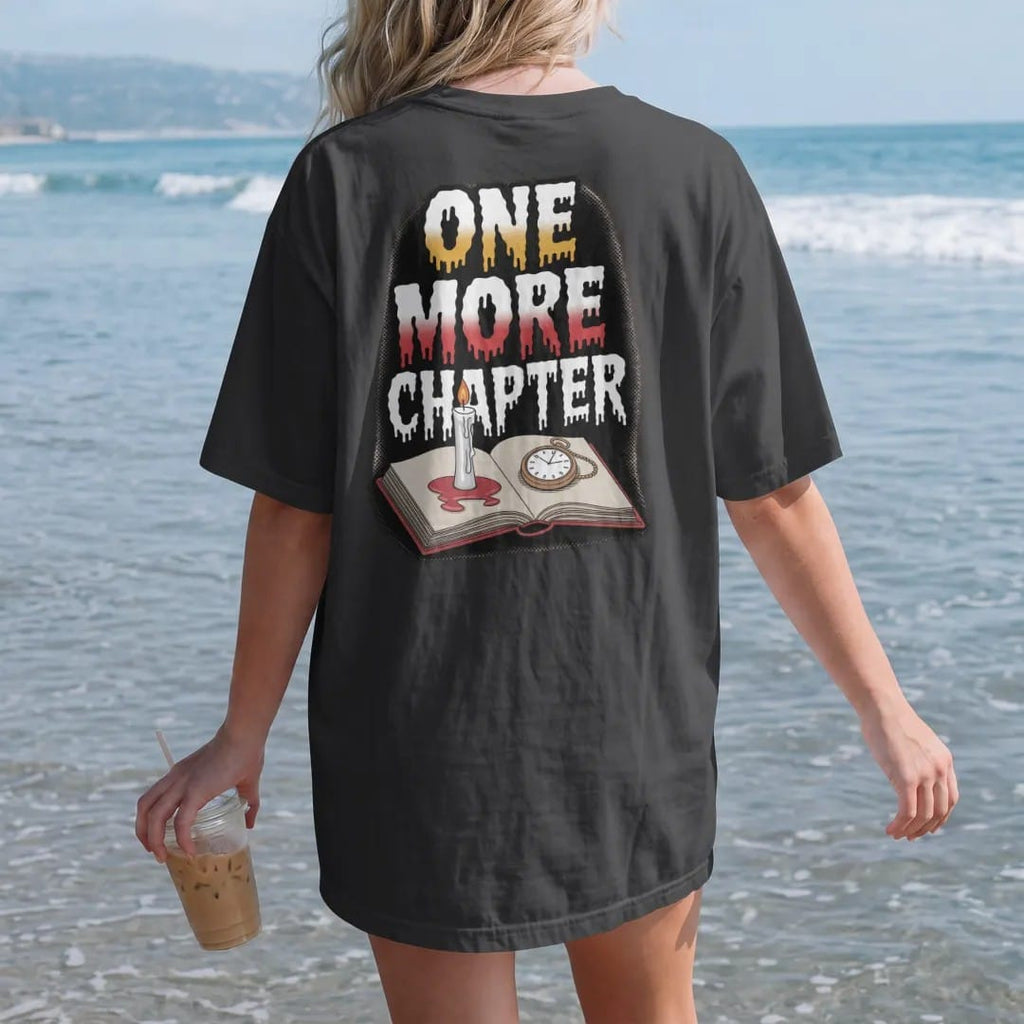 Woman on the beach in a Black tee, back view: a melted candle stub on an open book next to a cracked pocket watch with One More Chapter stacked above and below, in pulp halftone cream, red, yellow and blue.