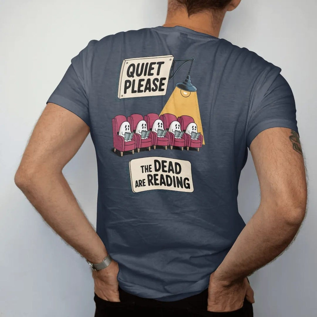 Man wearing a Midnight tee, seen from the back: a library placard reading Quiet Please over a row of small ghosts reading in armchairs, with The Dead Are Reading below, in pulp halftone cream, red, yellow and blue.