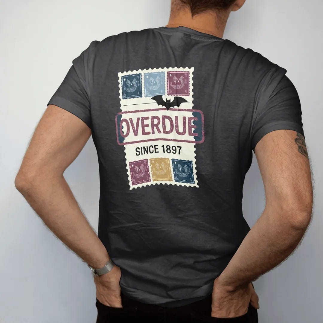 Man wearing a Black tee, seen from the back: a vintage library due-date card with a big slanted Overdue stamp, Since 1897 stamped below and a small bat clipped on, in pulp halftone navy, red, mustard and teal.