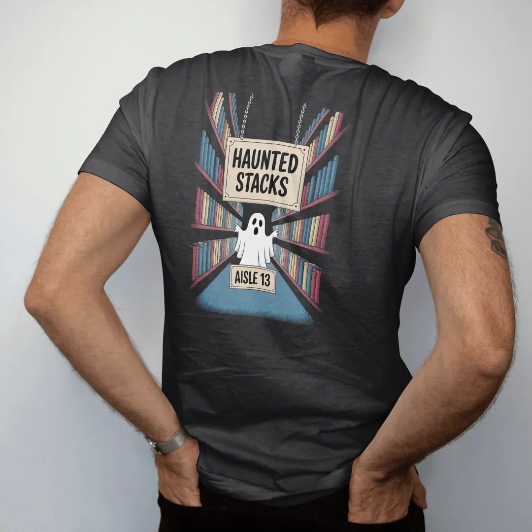 Man wearing a Black tee, seen from the back: a hanging aisle sign reading Haunted Stacks over a ghost peeking between foggy bookshelves, with an Aisle 13 plate, in pulp halftone cream, red, yellow and blue.