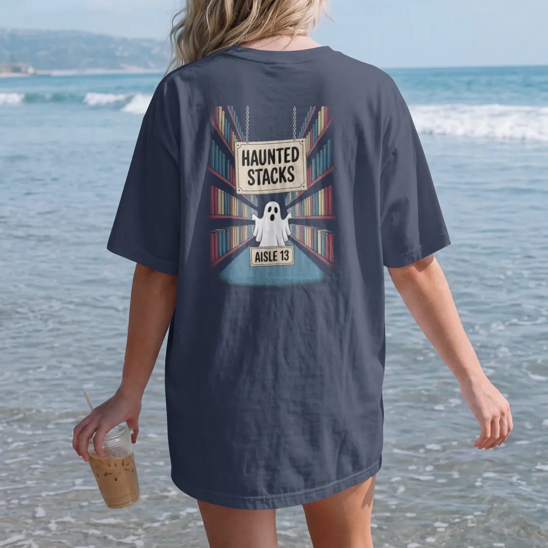 Woman on the beach in a Navy tee, back view: a hanging aisle sign reading Haunted Stacks over a ghost peeking between foggy bookshelves, with an Aisle 13 plate, in pulp halftone cream, red, yellow and blue.