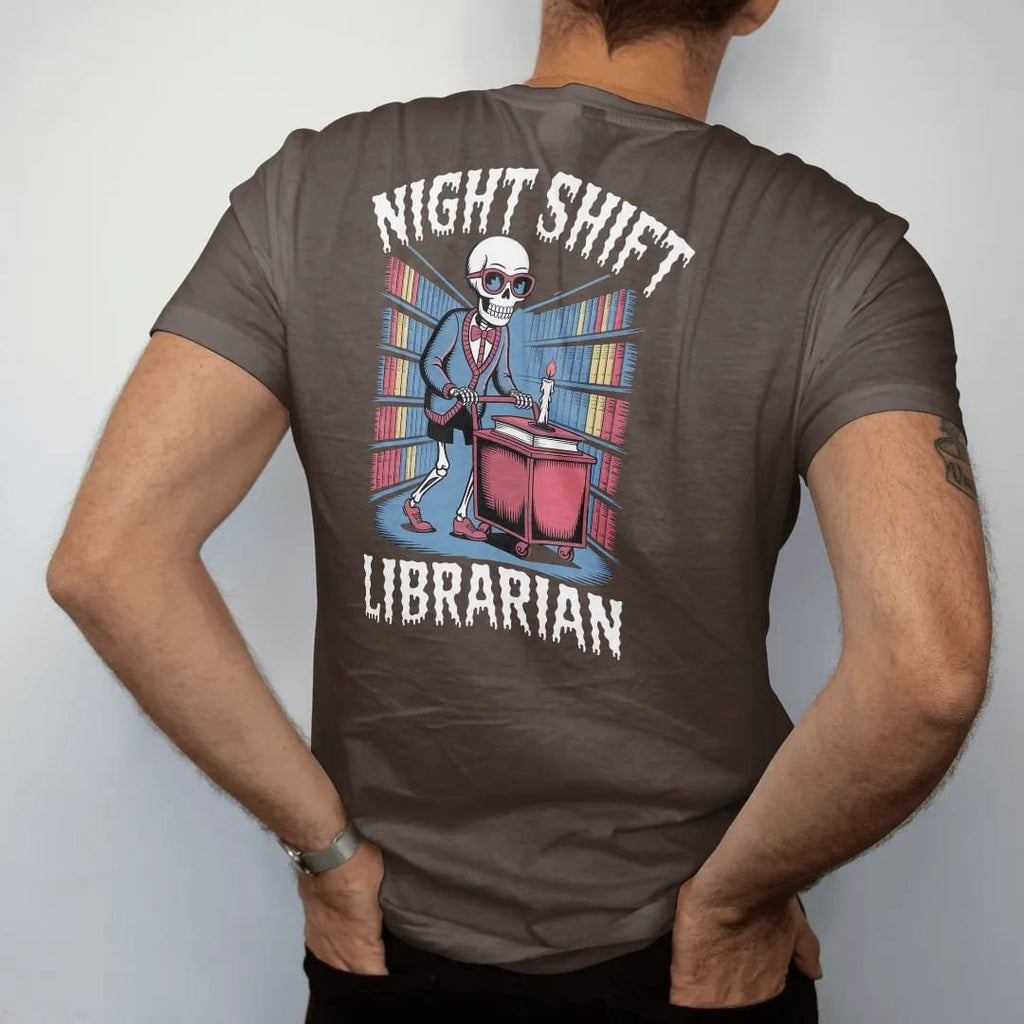 Man wearing a Espresso tee, seen from the back: a skeleton librarian in cat-eye glasses pushing a candlelit book cart through foggy stacks, with Night Shift above and Librarian below, in pulp halftone cream, red, yellow and blue.