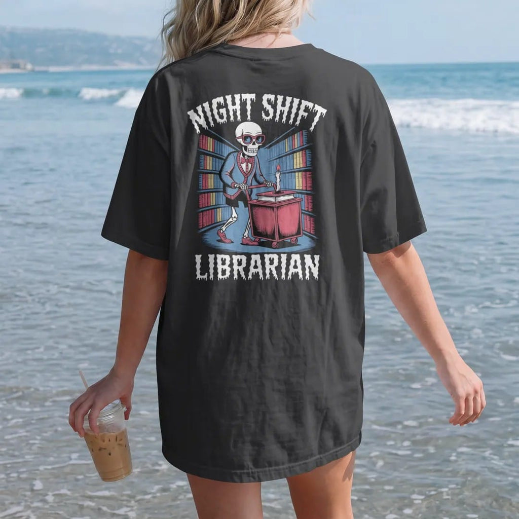Woman on the beach in a Black tee, back view: a skeleton librarian in cat-eye glasses pushing a candlelit book cart through foggy stacks, with Night Shift above and Librarian below, in pulp halftone cream, red, yellow and blue.