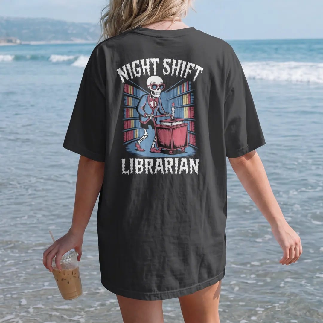 Woman on the beach in a Black tee, back view: a skeleton librarian in cat-eye glasses pushing a candlelit book cart through foggy stacks, with Night Shift above and Librarian below, in pulp halftone cream, red, yellow and blue.