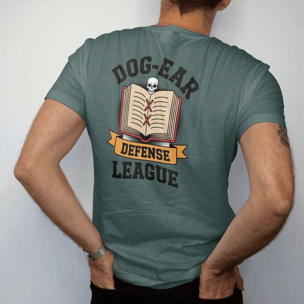 Man wearing a Blue Spruce tee, seen from the back: a crest of a book with folded page corners and broken bookmarks under a small skull, Dog-Ear arched above and a Defense League ribbon, in pulp halftone cream, red, yellow and blue.