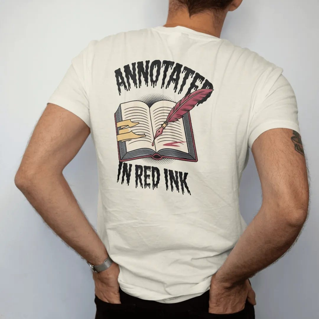 Man wearing a Ivory tee, seen from the back: an annotated open book full of tabs with a dripping quill leaning on it, Annotated above and In Red Ink below, in pulp halftone cream, red, yellow and blue.