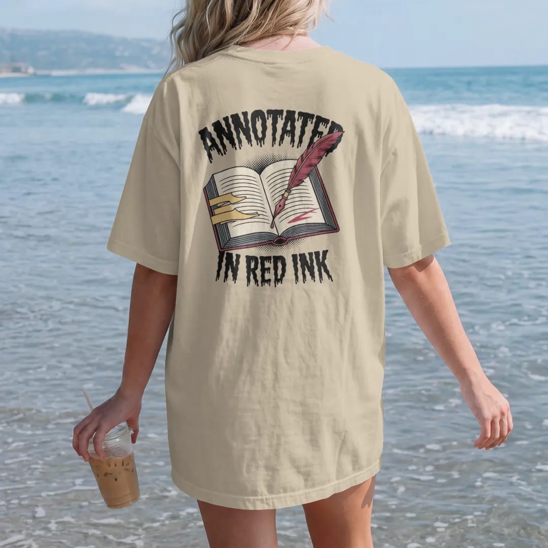 Woman on the beach in a Sandstone tee, back view: an annotated open book full of tabs with a dripping quill leaning on it, Annotated above and In Red Ink below, in pulp halftone cream, red, yellow and blue.