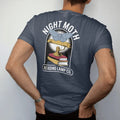 Man wearing a Midnight tee, seen from the back: a large moth circling a brass reading lamp over a book stack, Night Moth arched above and Reading Lamp Co. on a bar below, in pulp halftone cream, red, yellow and blue.