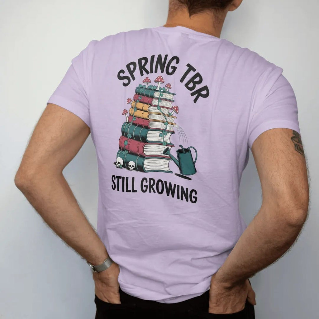Man wearing a Orchid tee, seen from the back: a tall book stack sprouting vines, mushrooms and skull flowers beside a tipped watering can, Spring TBR above and Still Growing below, in pulp halftone navy, red, mustard and teal.