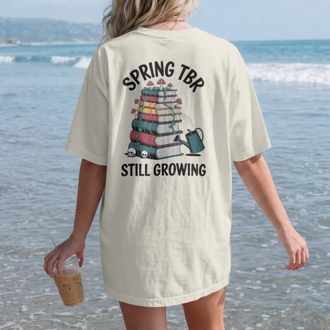 Woman on the beach in a Ivory tee, back view: a tall book stack sprouting vines, mushrooms and skull flowers beside a tipped watering can, Spring TBR above and Still Growing below, in pulp halftone navy, red, mustard and teal.