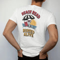 Man wearing a White tee, seen from the back: a skeleton in sunglasses half buried in sand under a beach umbrella reading a horror paperback, with Beach Read above and Buried Alive below, in pulp halftone cream, red, yellow and blue.