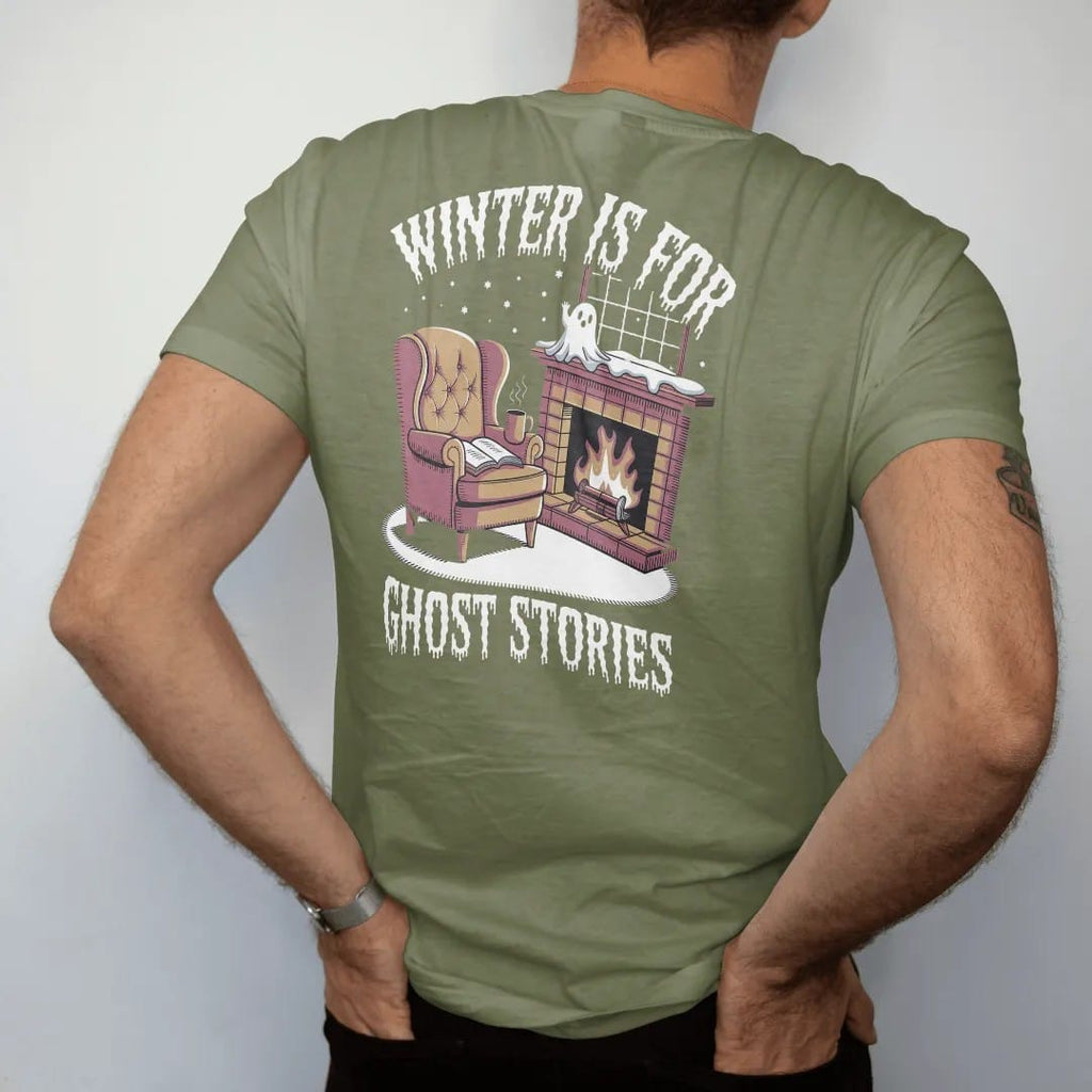 Man wearing a Moss tee, seen from the back: a wingback armchair by a fireplace with a book, steaming mug and a small ghost warming its hands, with Winter Is For above and Ghost Stories below, in pulp halftone cream, red, yellow and blue.