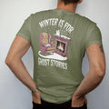 Man wearing a Moss tee, seen from the back: a wingback armchair by a fireplace with a book, steaming mug and a small ghost warming its hands, with Winter Is For above and Ghost Stories below, in pulp halftone cream, red, yellow and blue.
