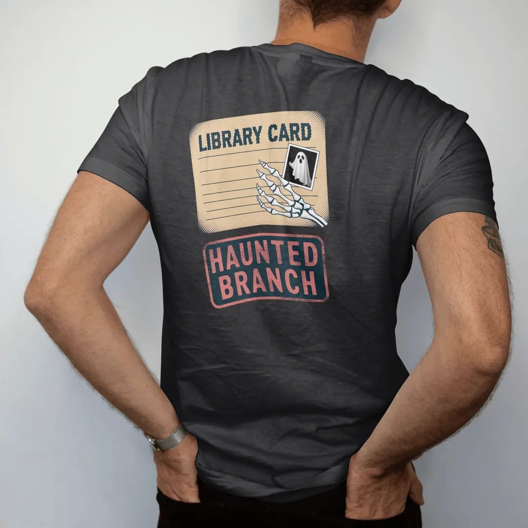 Man wearing a Black tee, seen from the back: a skeleton hand holding an old library card with a small ghost photo, Library Card across the top and Haunted Branch stamped below, in pulp halftone navy, red, mustard and teal.