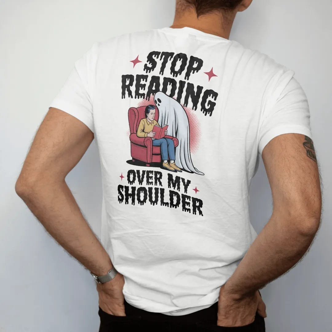 Man wearing a White tee, seen from the back: a pale ghost leaning over a reader's shoulder in an armchair, with Stop Reading above and Over My Shoulder below, in pulp halftone cream, red, yellow and blue.