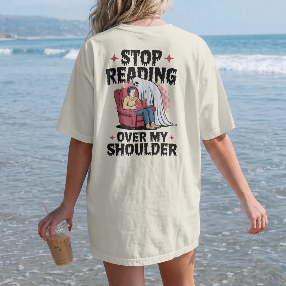 Woman on the beach in a Ivory tee, back view: a pale ghost leaning over a reader's shoulder in an armchair, with Stop Reading above and Over My Shoulder below, in pulp halftone cream, red, yellow and blue.