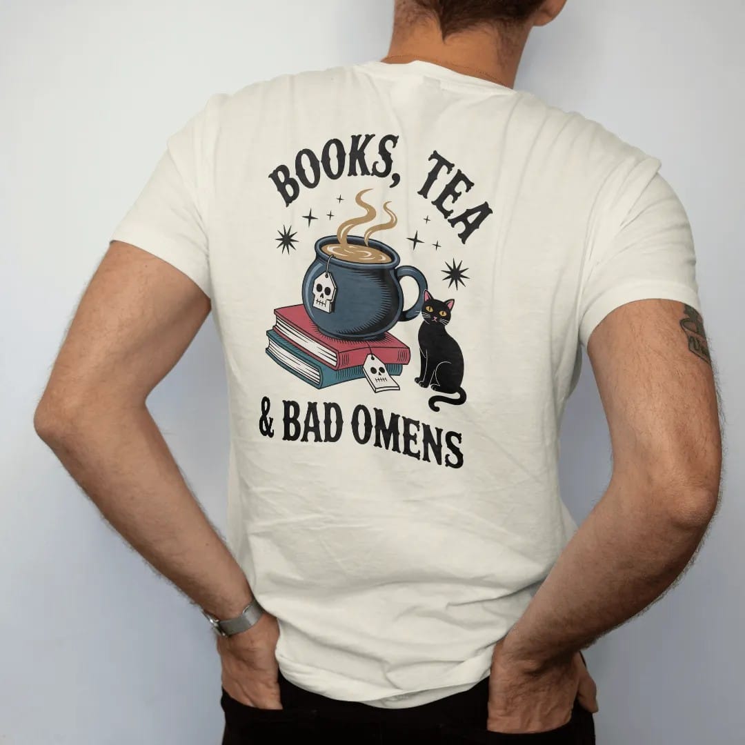 Man wearing a Ivory tee, seen from the back: a cauldron teacup with a skull tea tag beside a book stack and black cat, Books, Tea arched above and & Bad Omens below, in pulp halftone navy, red, mustard and teal.