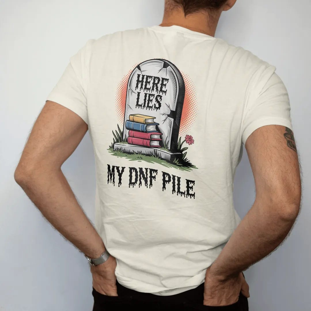 Man wearing a Ivory tee, seen from the back: a cracked tombstone carved Here Lies over a small pile of buried books with My DNF Pile below, in pulp halftone cream, red, yellow and blue.