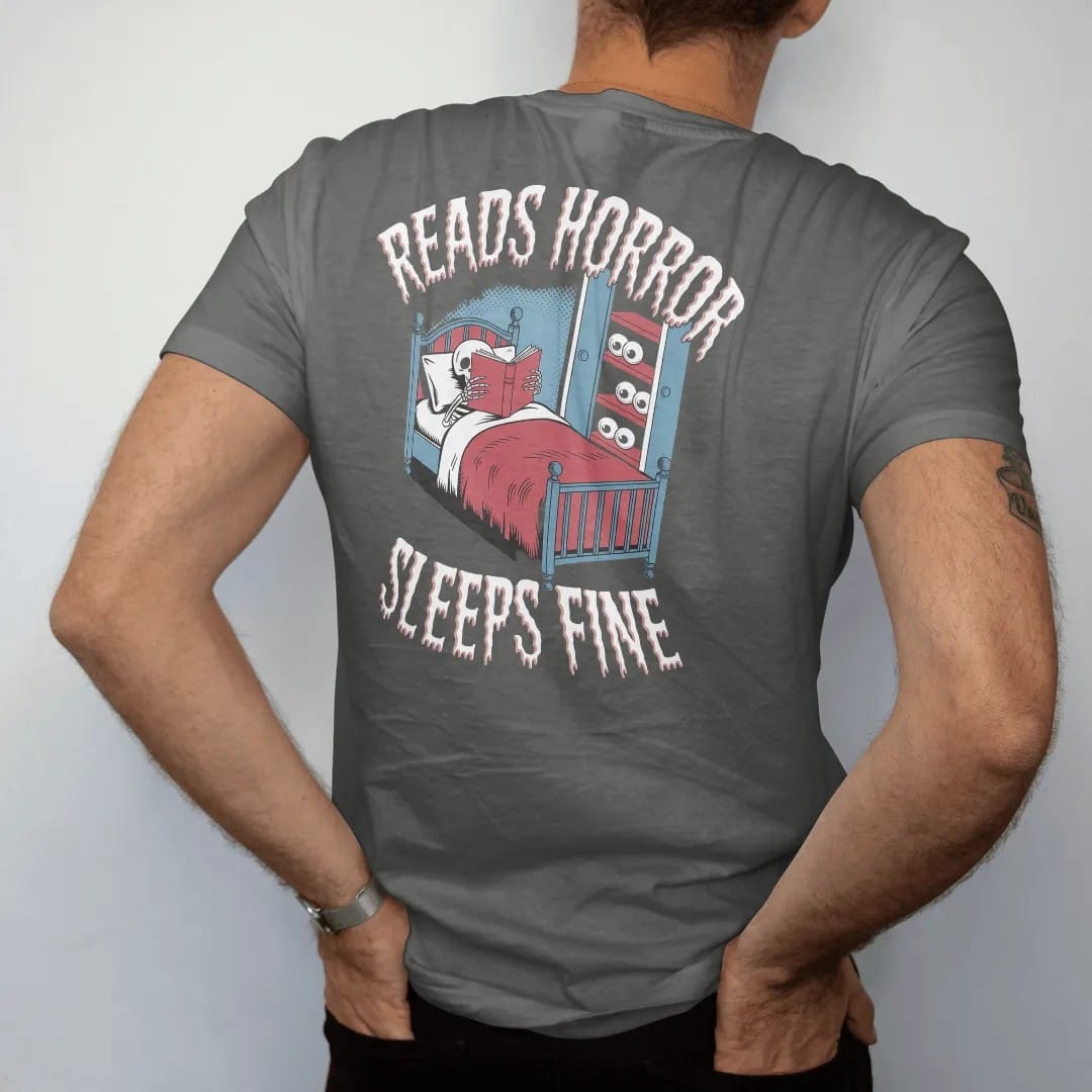 Man wearing a Pepper tee, seen from the back: a skeleton asleep with a horror book over its face while eyes peek from under the bed and closet, with Reads Horror above and Sleeps Fine below, in pulp halftone cream, red, yellow and blue.