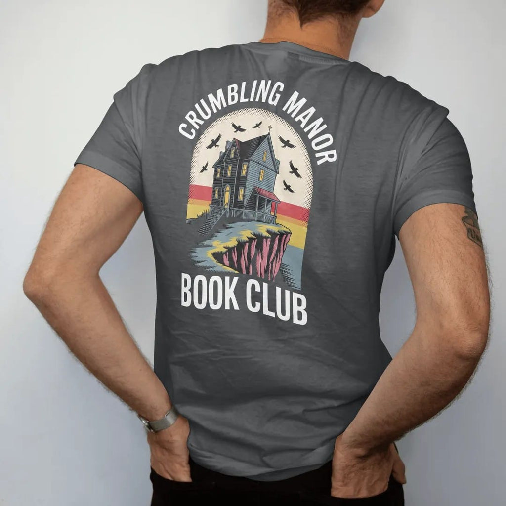 Man wearing a Graphite tee, seen from the back: a crumbling gothic manor on a cliff with one lit window and ravens circling, Crumbling Manor arched above and Book Club below, in pulp halftone cream, red, yellow and blue.