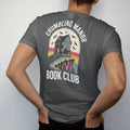 Man wearing a Graphite tee, seen from the back: a crumbling gothic manor on a cliff with one lit window and ravens circling, Crumbling Manor arched above and Book Club below, in pulp halftone cream, red, yellow and blue.