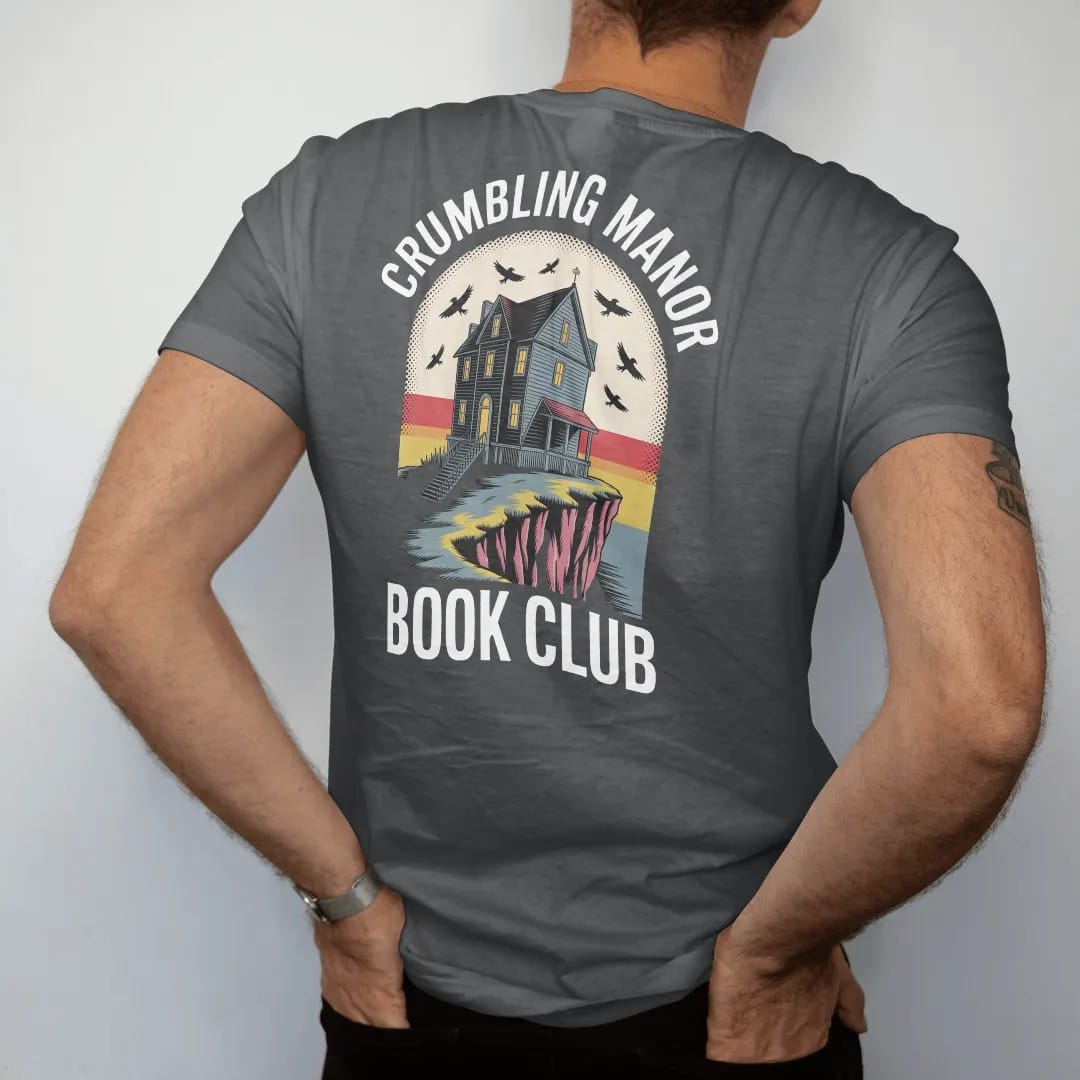Man wearing a Graphite tee, seen from the back: a crumbling gothic manor on a cliff with one lit window and ravens circling, Crumbling Manor arched above and Book Club below, in pulp halftone cream, red, yellow and blue.
