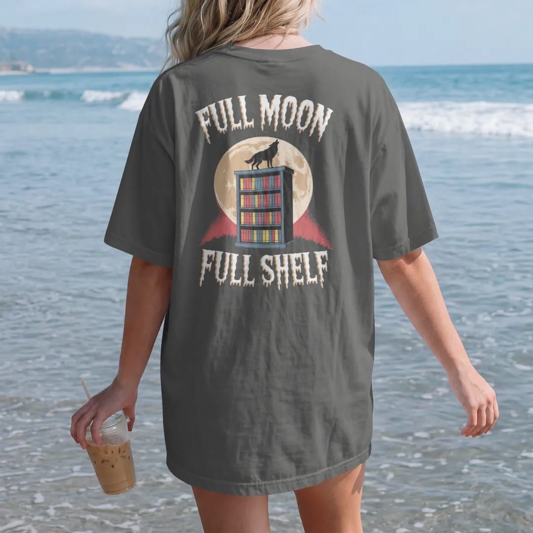 Woman on the beach in a Pepper tee, back view: a full moon behind a bookshelf on a hill with a wolf howling on top, with Full Moon above and Full Shelf below, in pulp halftone cream, red, yellow and blue.