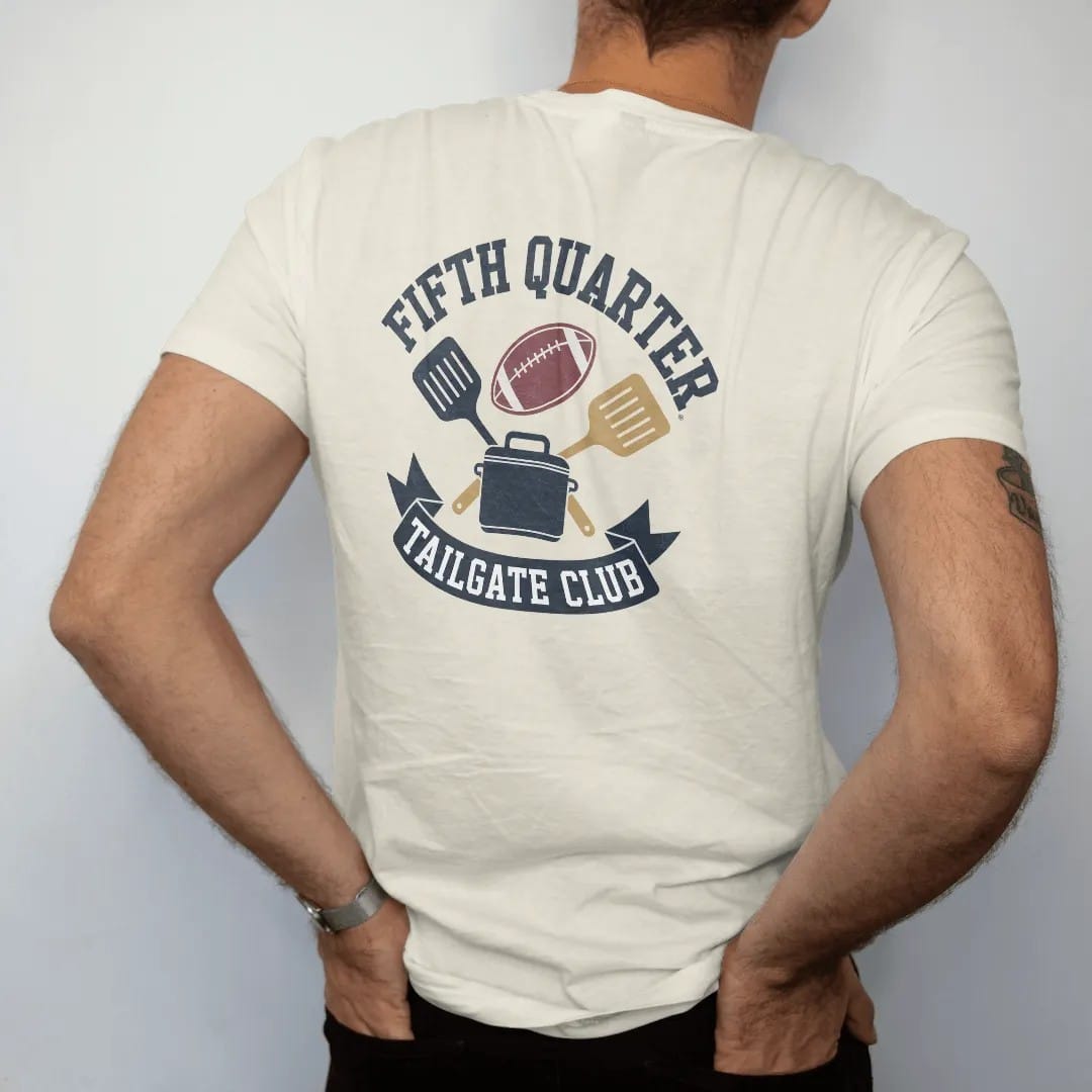Man wearing a Ivory tee, seen from the back: a crest with a football, crossed grilling spatulas and a cooler, with "FIFTH QUARTER" and "TAILGATE CLUB" in chunky rounded 70s varsity letters, printed in faded stadium green, washed brick red, faded…