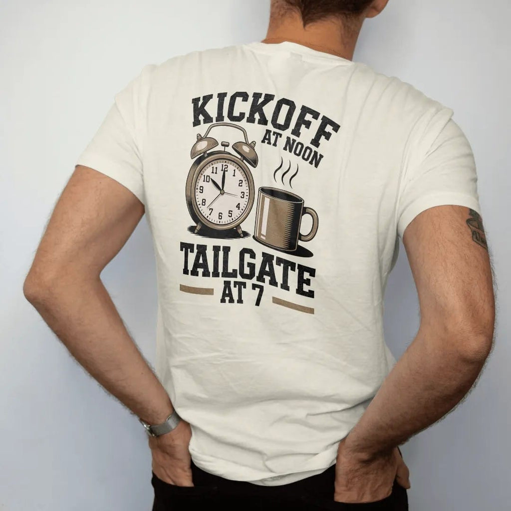 Man wearing a Ivory tee, seen from the back: a vintage alarm clock with a football face beside a steaming coffee mug, with "KICKOFF AT NOON" and "TAILGATE AT 7" in chunky 70s slab-serif letters, printed in faded stadium green, washed brick red,…
