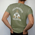 Man wearing a Moss tee, seen from the back: a fan bundled in a knit pom hat and blanket holding a steaming cup of chili as snow falls, with "COLD WEATHER" and "TAILGATER" in chunky rounded 70s varsity letters, printed in faded bleacher cream,…