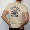 Man wearing a Sandstone tee, seen from the back: a vintage pickup truck with a grill in the bed and a pennant flying, with "GRANDPA'S TAILGATE" and "SINCE 1972" in chunky 1970s swash script, printed in faded stadium green, washed brick red, faded…