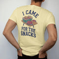 Man wearing a Butter tee, seen from the back: a loaded tailgate table with sliders, chips, dips and wings, with "I CAME" and "FOR THE SNACKS" in chunky 70s slab-serif letters, printed in faded stadium green, washed brick red, faded navy and mustard…
