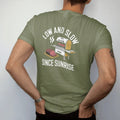 Man wearing a Moss tee, seen from the back: a smoker cabinet puffing smoke beside a sliced brisket on a cutting board, with "LOW AND SLOW" and "SINCE SUNRISE" in chunky 70s slab-serif letters, printed in faded bleacher cream, mustard, washed tomato…