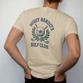 Man wearing a Sandstone tee, seen from the back: a golf ball in a bandit eye mask over crossed clubs and a laurel wreath, with "BOGEY BANDITS" and "GOLF CLUB" in chunky rounded 70s serif letters, printed in faded fairway green, washed navy, faded…