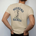 Man wearing a Sandstone tee, seen from the back: a golfer mid swing with a big chunk of turf flying up, with "WEEKEND" and "HACKER" in loopy 1970s script, printed in faded fairway green, washed navy, faded flag red and sand tan with a cracked, worn…