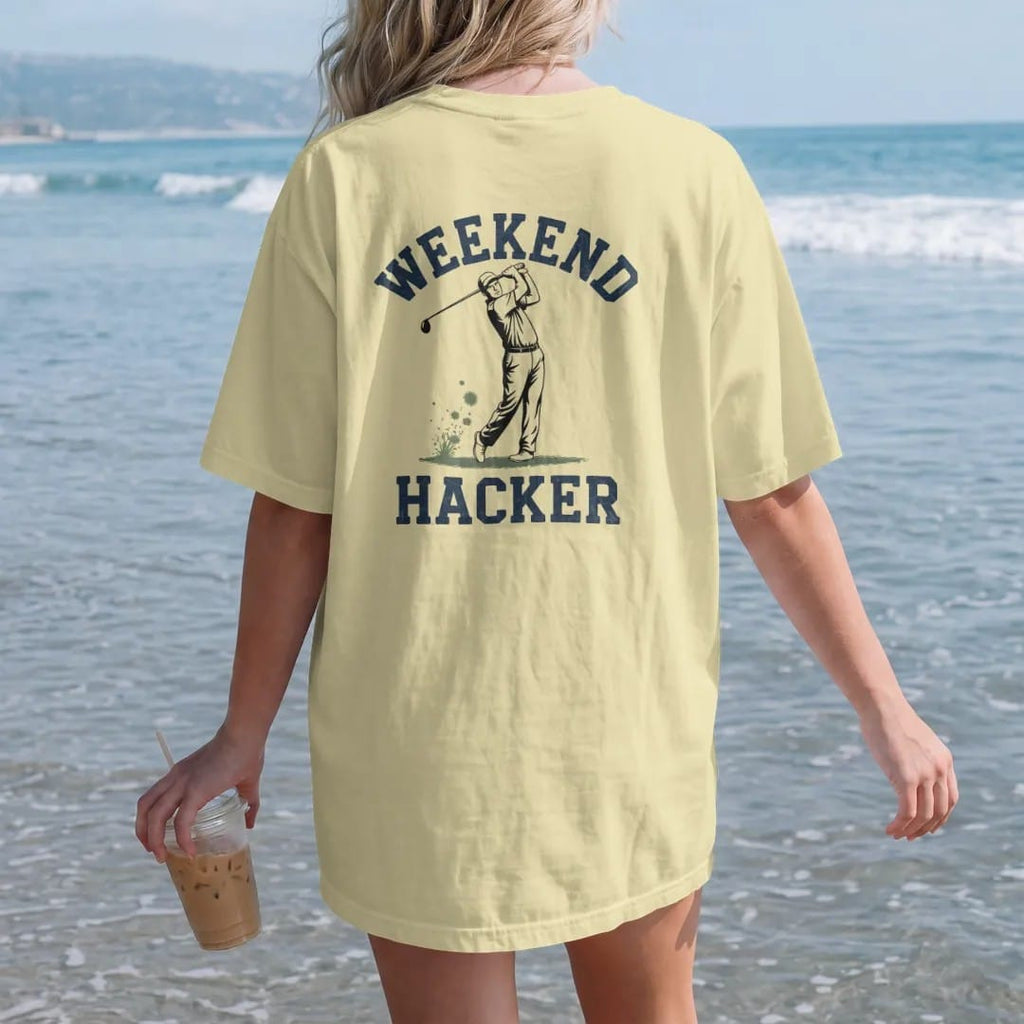 Woman on the beach in a Butter tee, back view: a golfer mid swing with a big chunk of turf flying up, with "WEEKEND" and "HACKER" in loopy 1970s script, printed in faded fairway green, washed navy, faded flag red and sand tan with a cracked, worn…