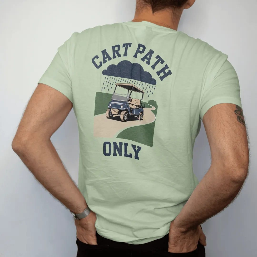 Man wearing a Light Green tee, seen from the back: a vintage golf cart puttering along a winding path under rain clouds, with "CART PATH" and "ONLY" in chunky rounded 70s serif letters, printed in faded fairway green, washed navy, faded flag red…