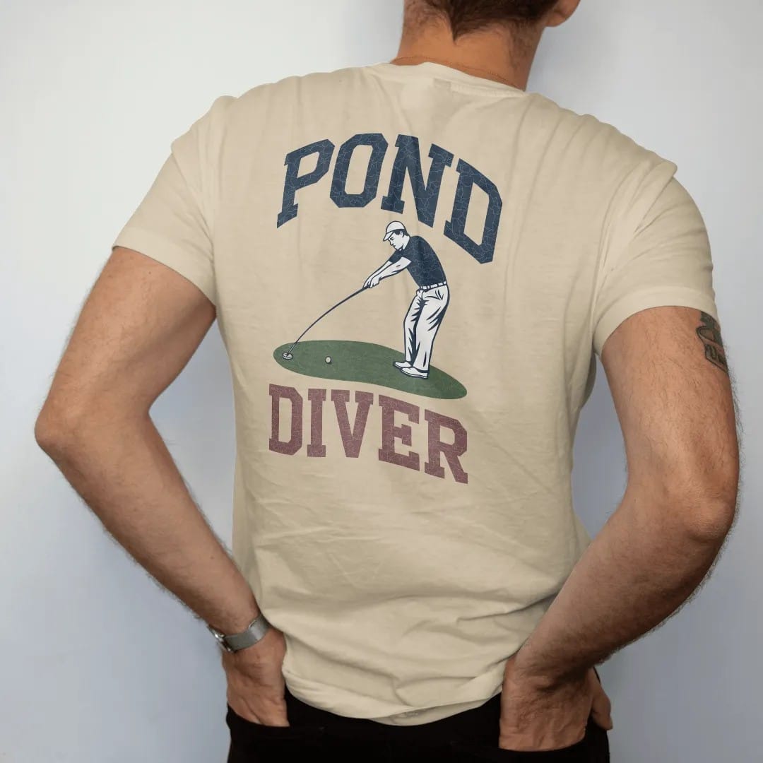Man wearing a Sandstone tee, seen from the back: a golfer stretching a long ball-retriever pole to fish a ball out of a pond, with "POND" and "DIVER" in chunky faded collegiate block letters, printed in faded fairway green, washed navy, faded flag…