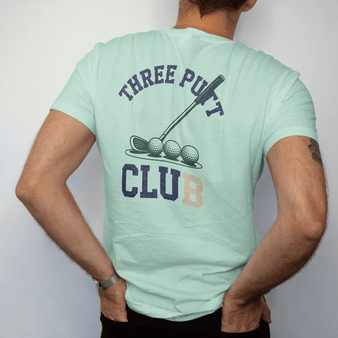 Man wearing a Chalky Mint tee, seen from the back: a putter and three golf balls in a row near the cup, with "THREE PUTT" and "CLUB" in chunky faded collegiate block letters, printed in faded fairway green, washed navy, faded flag red and sand tan…