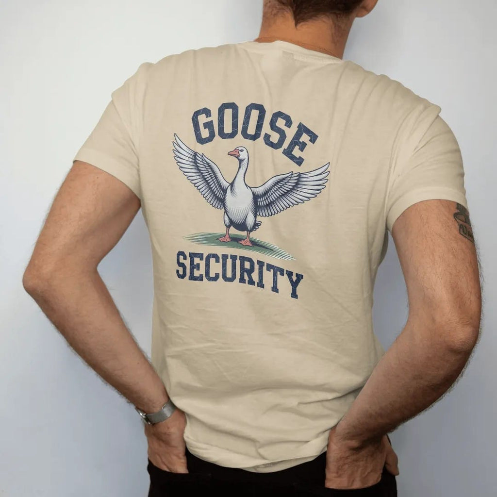 Man wearing a Sandstone tee, seen from the back: an angry goose with wings spread wide on a fairway, with "GOOSE" and "SECURITY" in chunky faded collegiate block letters, printed in faded fairway green, washed navy, faded flag red and sand tan with…