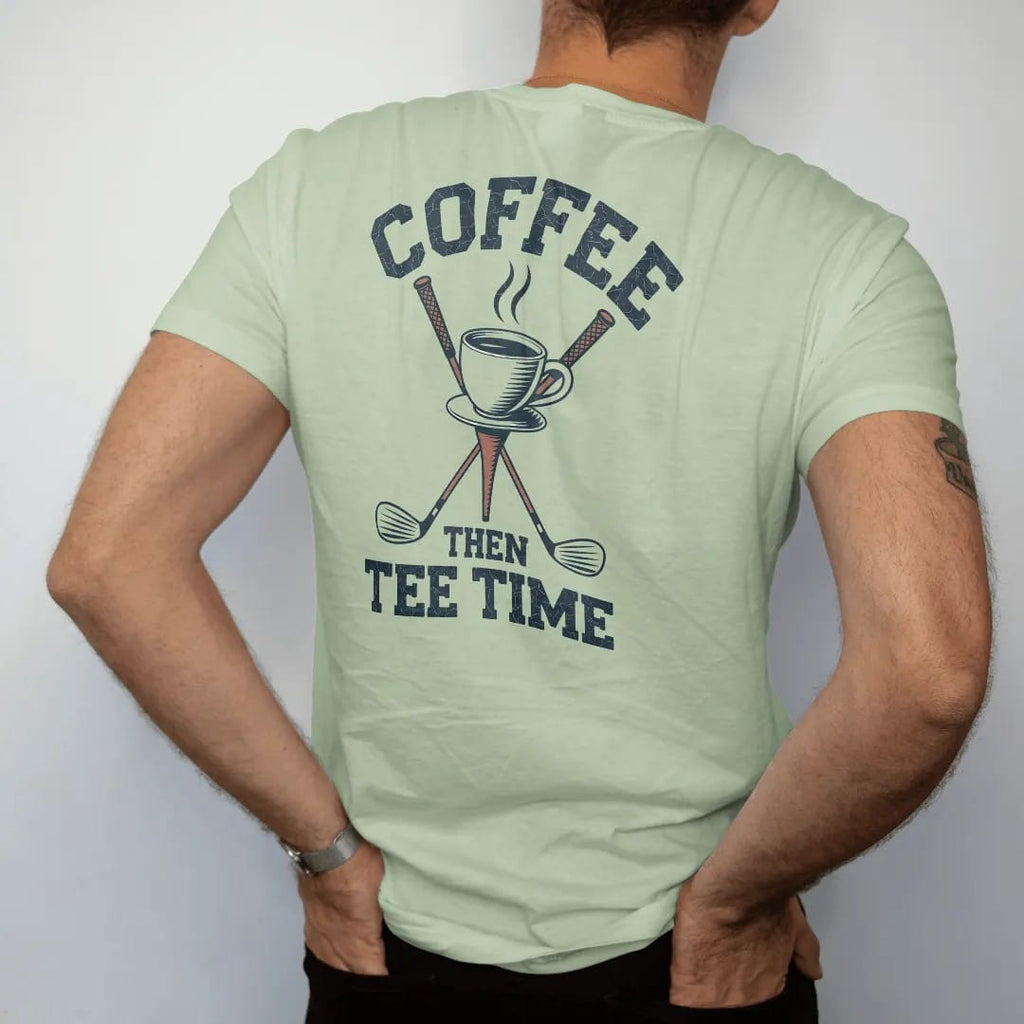 Man wearing a Light Green tee, seen from the back: a steaming coffee cup balanced on a golf tee with clubs behind, with "COFFEE" and "THEN TEE TIME" in loopy 1970s script, printed in faded fairway green, washed navy, faded flag red and sand tan…