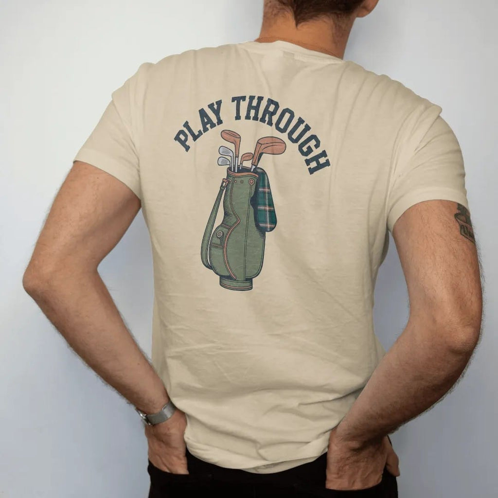 Man wearing a Sandstone tee, seen from the back: a vintage leather golf bag with wooden-headed clubs and a tartan headcover, with "PLAY THROUGH" in chunky rounded 70s serif letters, printed in faded fairway green, washed navy, faded flag red and…