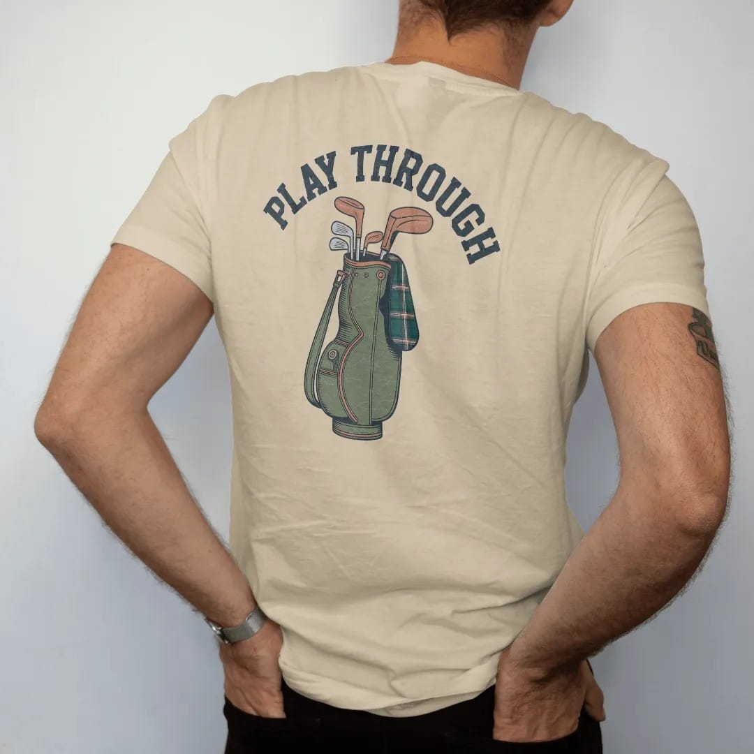 Man wearing a Sandstone tee, seen from the back: a vintage leather golf bag with wooden-headed clubs and a tartan headcover, with "PLAY THROUGH" in chunky rounded 70s serif letters, printed in faded fairway green, washed navy, faded flag red and…