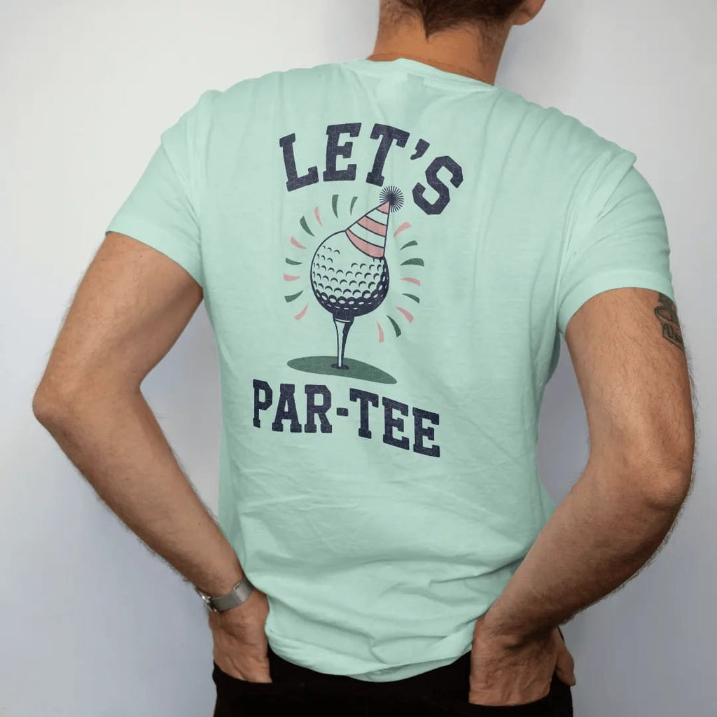 Man wearing a Chalky Mint tee, seen from the back: a golf ball on a tee wearing a party hat with confetti flying, with "LET'S" and "PAR-TEE" in loopy 1970s script, printed in faded fairway green, washed navy, faded flag red and sand tan with a…