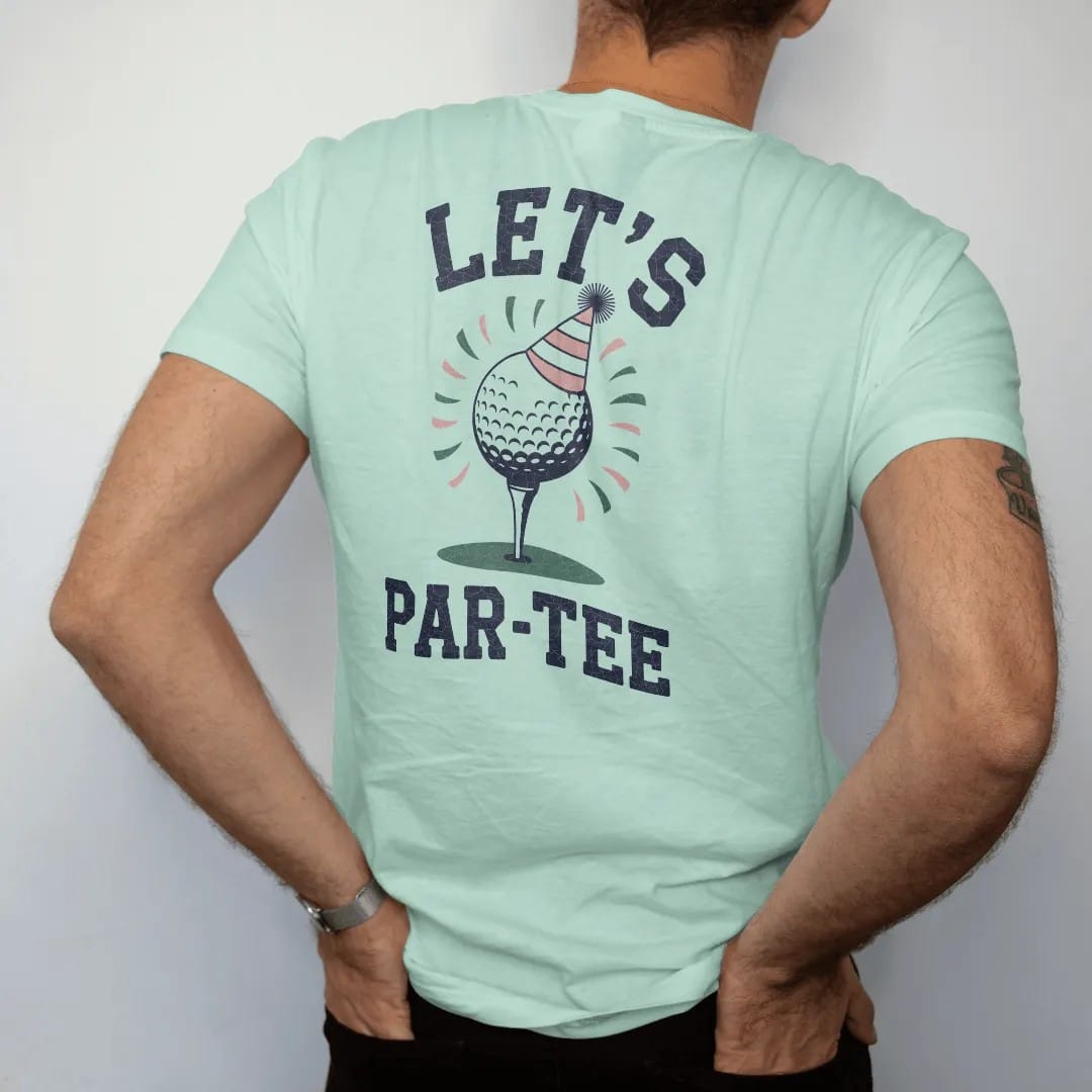 Man wearing a Chalky Mint tee, seen from the back: a golf ball on a tee wearing a party hat with confetti flying, with "LET'S" and "PAR-TEE" in loopy 1970s script, printed in faded fairway green, washed navy, faded flag red and sand tan with a…