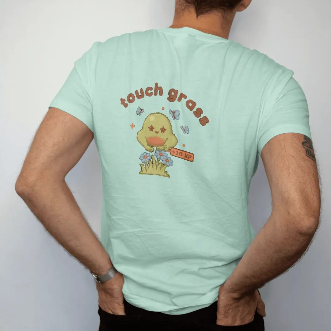 Man wearing a Chalky Mint tee, seen from the back: blip the pixel slime patting a tuft of grass and daisies under touch grass in rounded letters, with a +10 XP pixel popup, in moss green, rust and brown.
