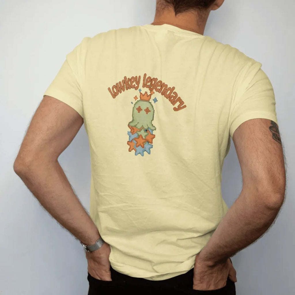 Man wearing a Butter tee, seen from the back: blip the pixel slime wearing a tilted crown on a stack of rarity stars, under lowkey legendary in brown, rust and moss wavy letters.