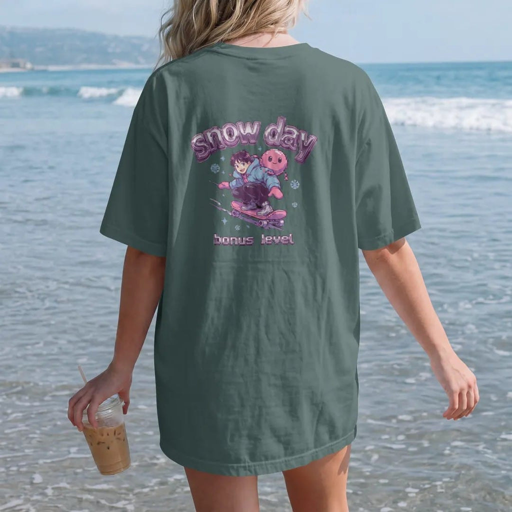 Woman on the beach in a Blue Spruce tee, back view: an anime-style kid sledding down a snowy hill on a skateboard with Blip the slime riding along, under snow day in frosty chrome letters and bonus level in pixel type, in ice blue, silver, lilac…