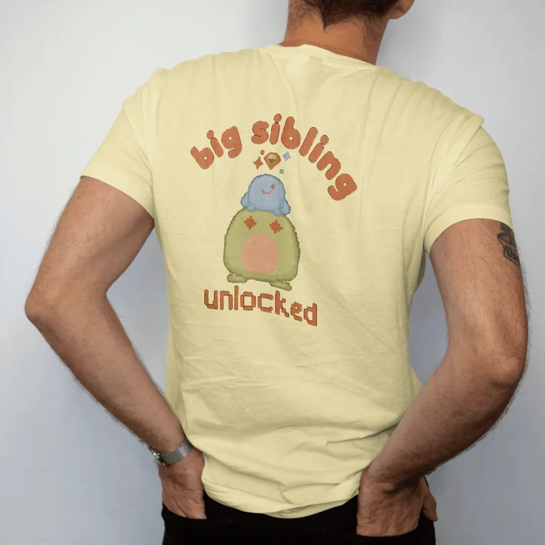 Man wearing a Butter tee, seen from the back: blip the pixel slime carrying a tiny baby slime under a quest marker and sparkles, with big sibling in rounded letters and unlocked in pixel type, in brown, rust, moss and denim.
