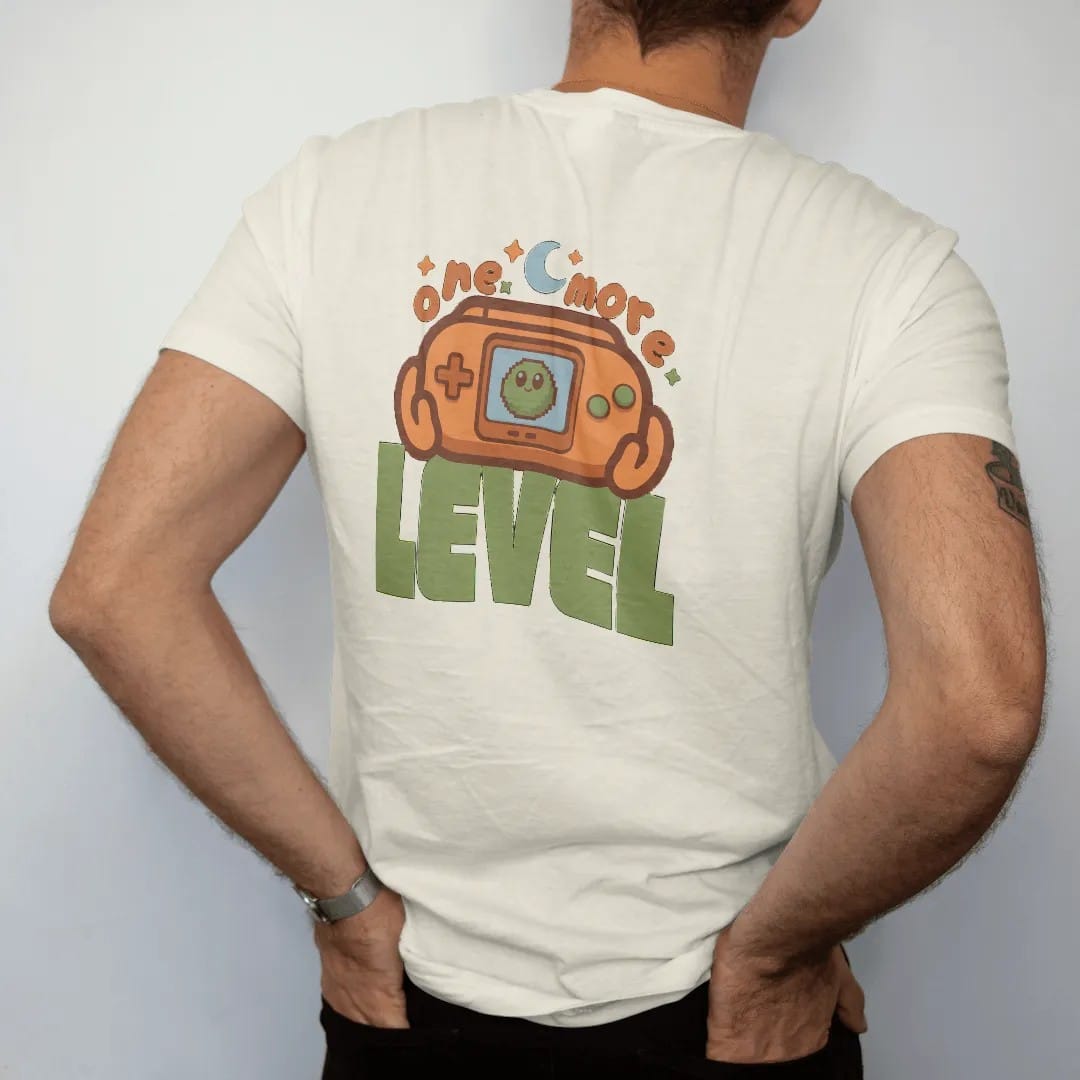 Man wearing a Ivory tee, seen from the back: a generic retro handheld console showing Blip the pixel slime, held under a moon and stars, with one more in arcade letters and level in big block type, in brown, rust, moss and denim.